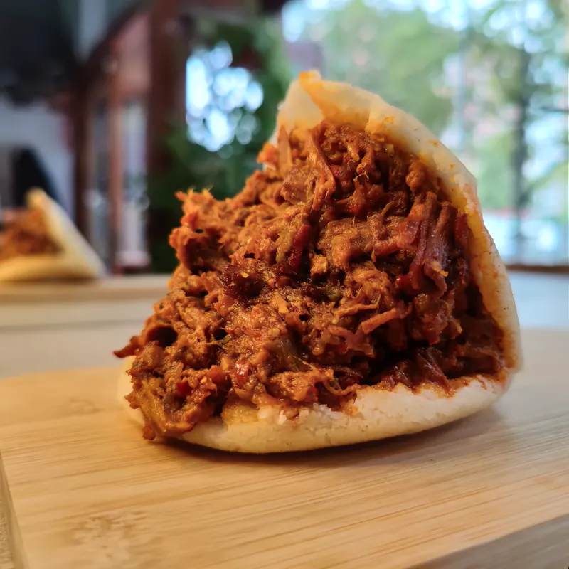 Arepa abierta con un relleno abundante de fibras rojizas.
