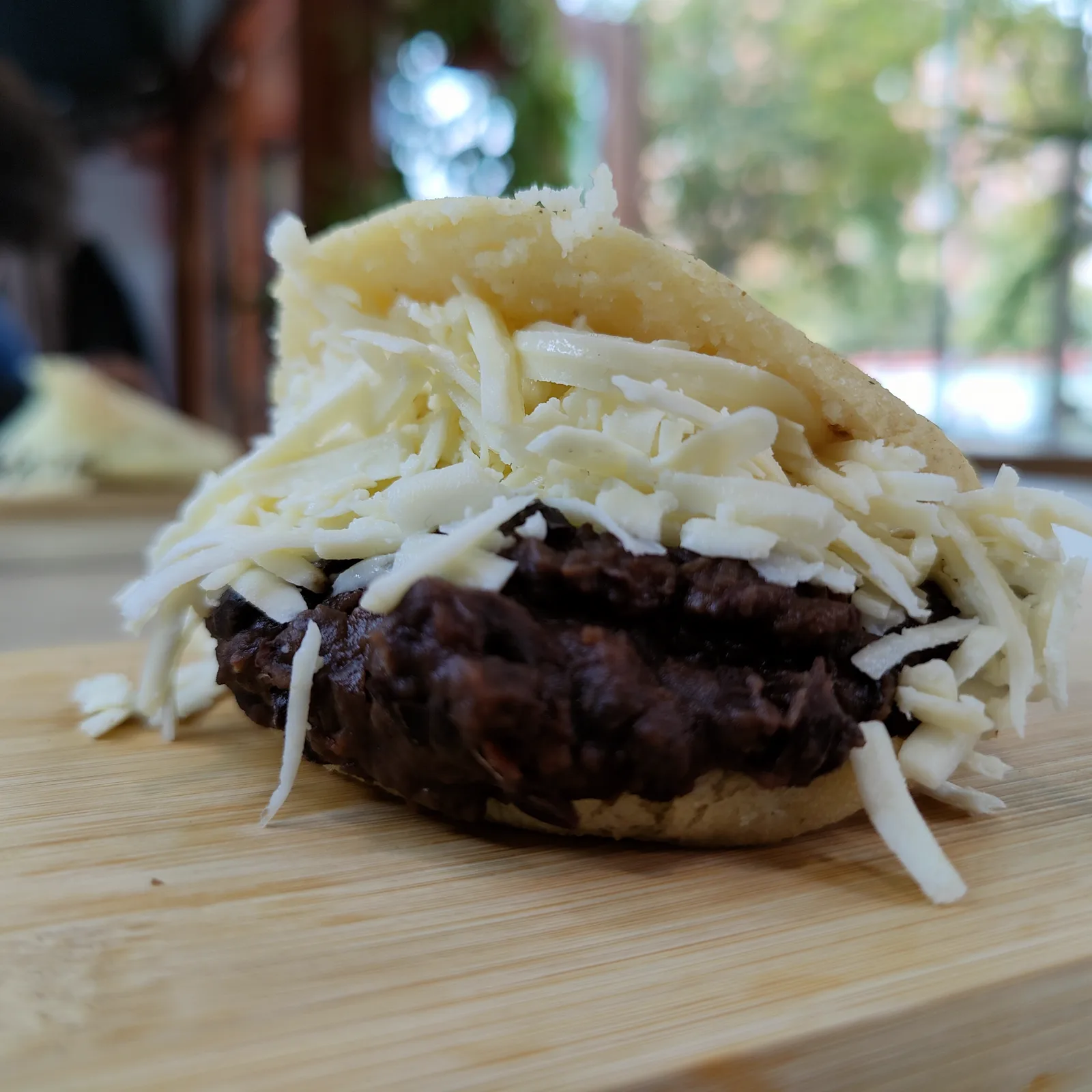 Arepa dominó abierta con relleno oscuro y queso blanco rallado.