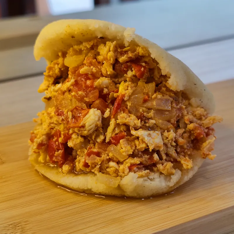 Arepa abierta con un relleno abundante de tonos amarillos y rojos.