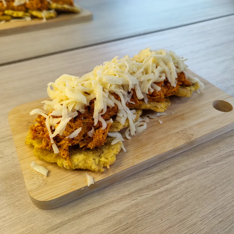 Preparación aplanada de plátano con relleno oscuro y queso blanco rallado.