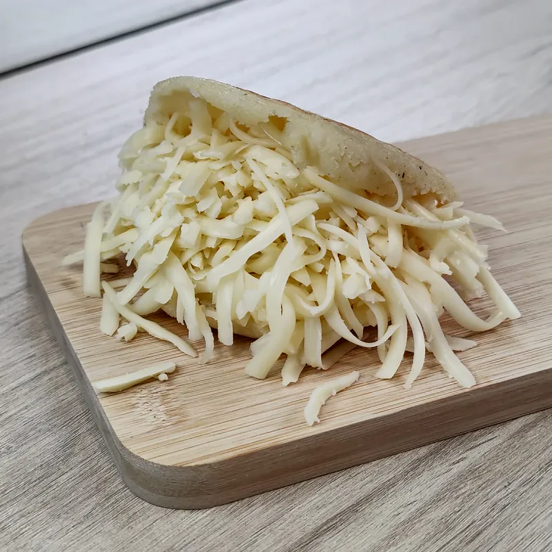 Arepa abierta con queso blanco rallado sobre una tabla.