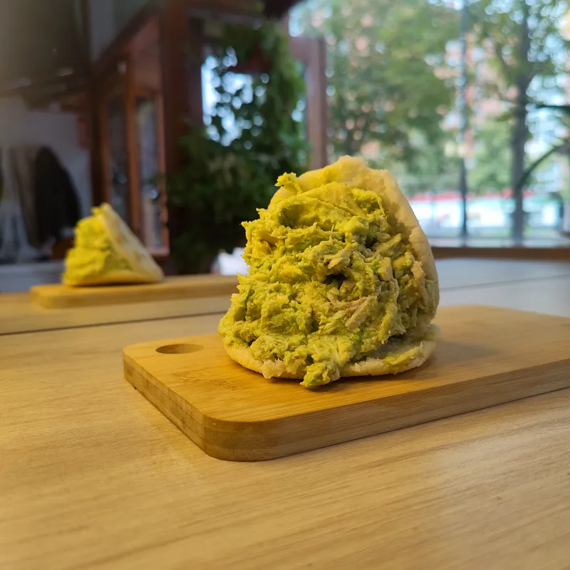 Arepa abierta con relleno cremoso verde sobre una tabla de madera.